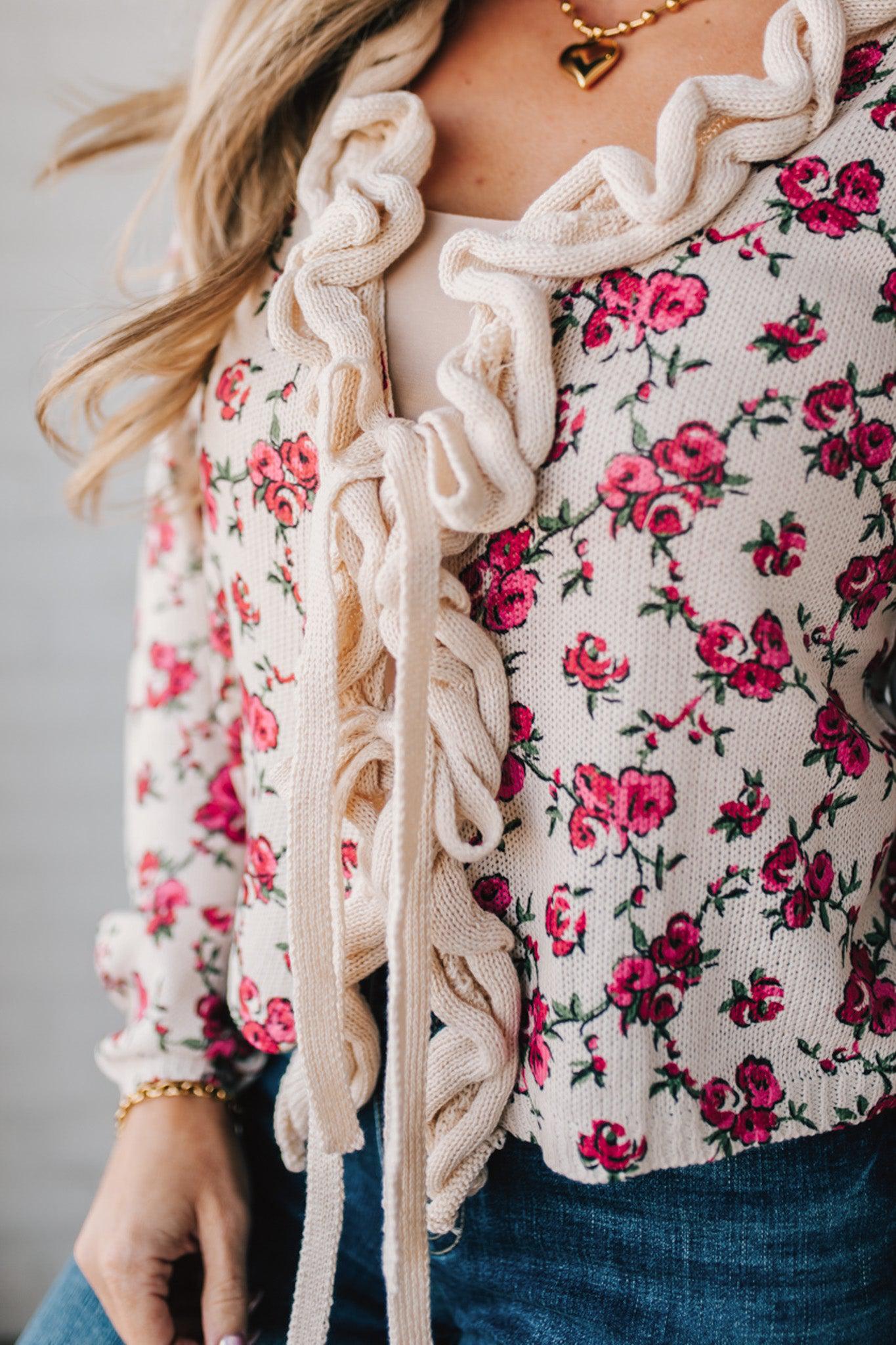 blonde girl modeling a long sleeve cream colored cardigan with a pink floral pattern and ruffle edge detail