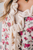 blonde girl modeling a long sleeve cream colored cardigan with a pink floral pattern and ruffle edge detail