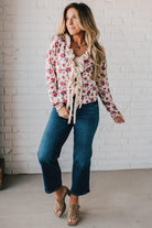 blonde girl modeling a long sleeve cream colored cardigan with a pink floral pattern and ruffle edge detail