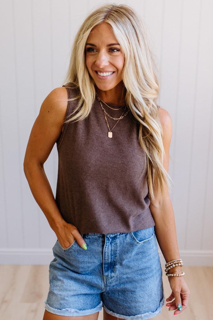 Woman wearing a brown sleeveless top and denim shorts with a neutral background