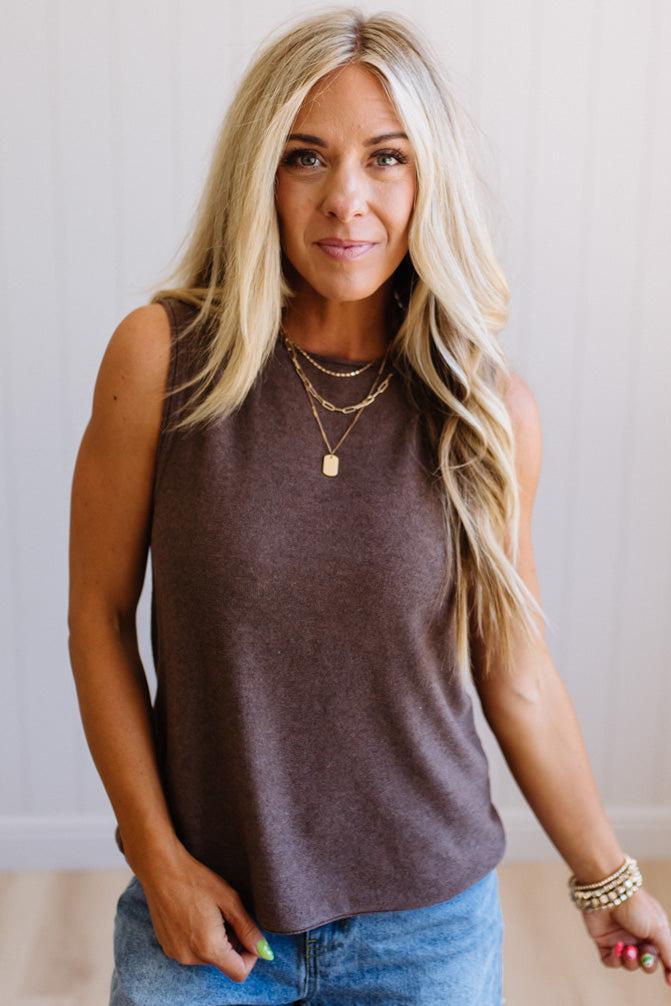 Woman wearing a brown sleeveless top and blue jeans with a neutral background