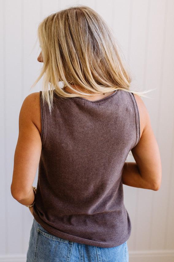Person wearing a brown tank top and blue jeans against a plain background