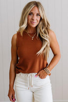 Woman wearing a brown sleeveless top and white pants against a light background