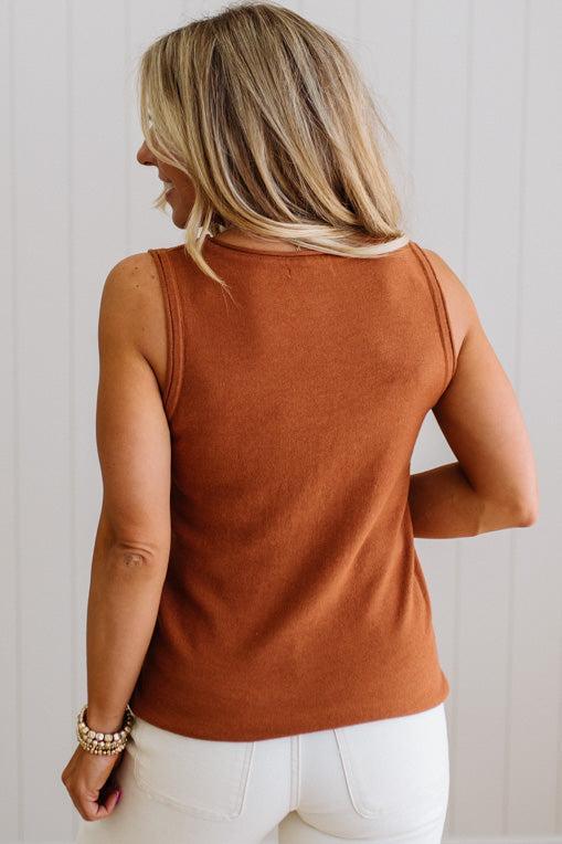 Woman wearing a rust-colored sleeveless top against a light background