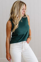 Woman wearing a green sleeveless top and white pants against a light background