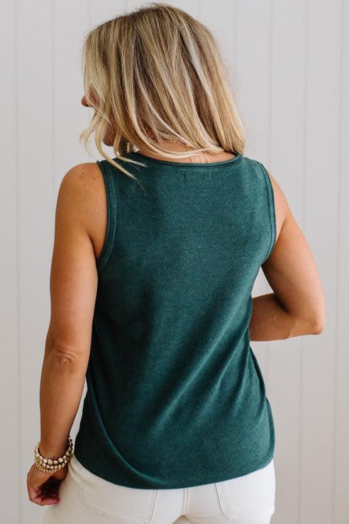 Person wearing a green sleeveless top and white pants against a light background