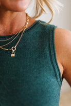 Person wearing a green sleeveless top and gold necklaces with lock pendants.
