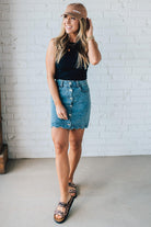 BLONDE WOMAN IN A HAT AND BLACK TANK WEARING A SCALLOP BUTTONED FRONT DENIM SKIRT.