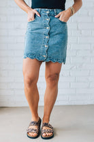 BLONDE WOMAN IN A HAT AND BLACK TANK WEARING A SCALLOP BUTTONED FRONT DENIM SKIRT.