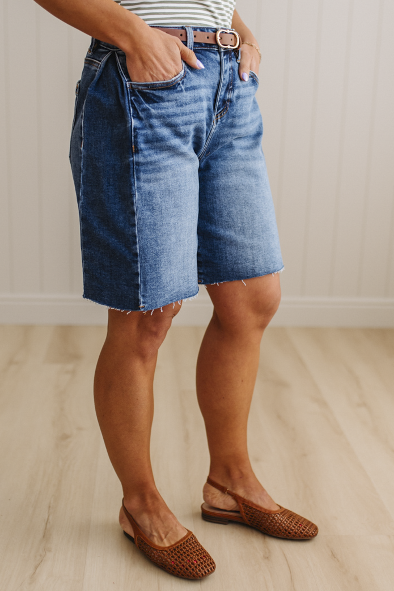 Person wearing blue denim shorts and brown sandals on a wooden floor.