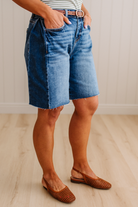 Person wearing blue denim shorts and brown sandals on a wooden floor.
