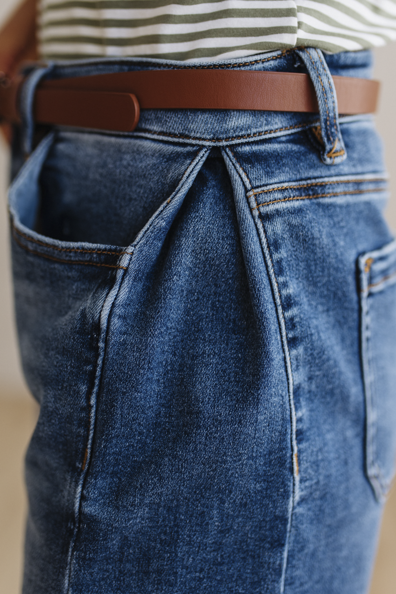 Close-up of blue jeans with a brown belt and striped shirt.