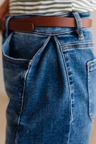 Close-up of blue jeans with a brown belt and striped shirt.