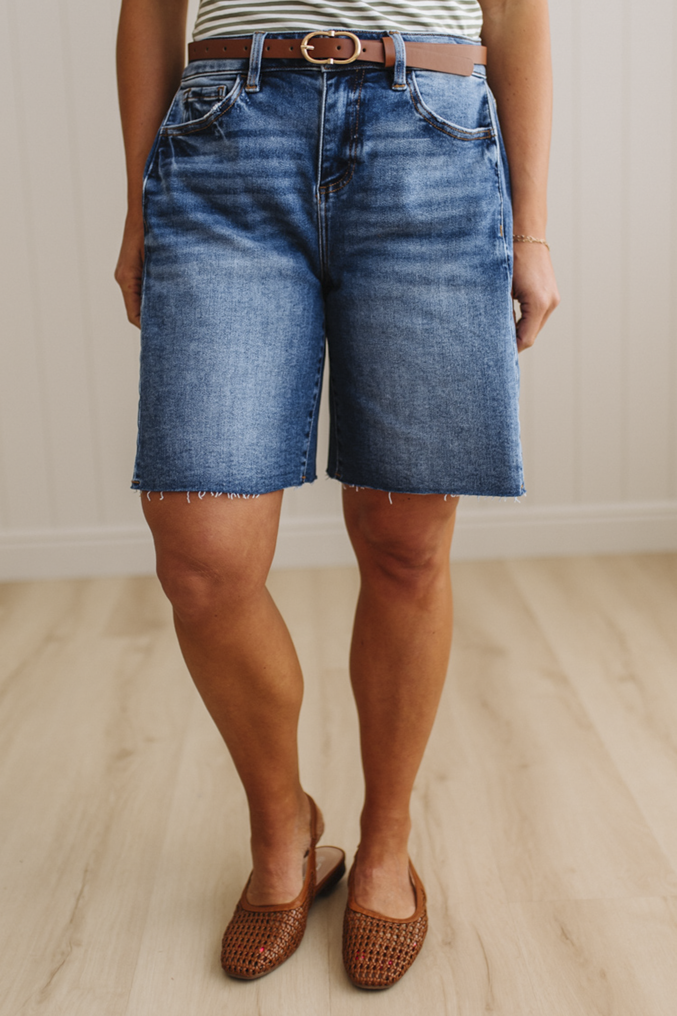 Person wearing blue denim shorts and brown sandals on a light wooden floor.