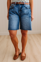 Person wearing blue denim shorts and brown sandals on a light wooden floor.