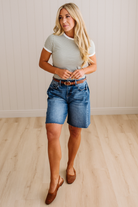 Woman wearing a striped shirt and denim shorts standing on a wooden floor.