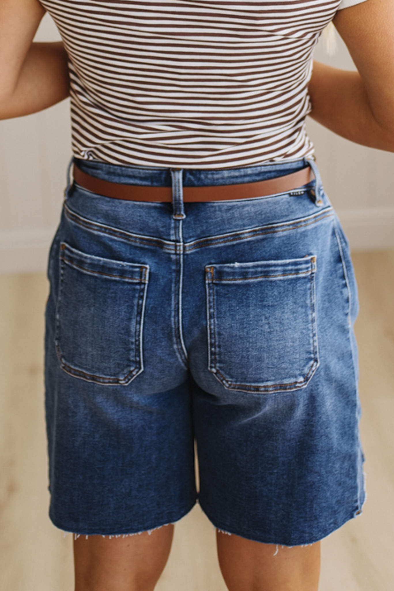 Person wearing a striped shirt and blue denim shorts with a blurred background