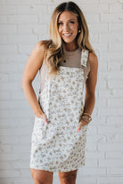 Blonde Woman Wearing a Stretch Ditsy Print Denim Overall Mini Dress in Cream and multi color flowers.