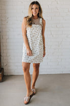 Blonde Woman Wearing a Stretch Ditsy Print Denim Overall Mini Dress in Cream and multi color flowers.