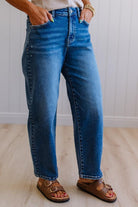 Person wearing blue jeans and brown sandals on a light wooden floor.