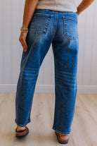 Person wearing blue jeans standing against a white paneled wall.