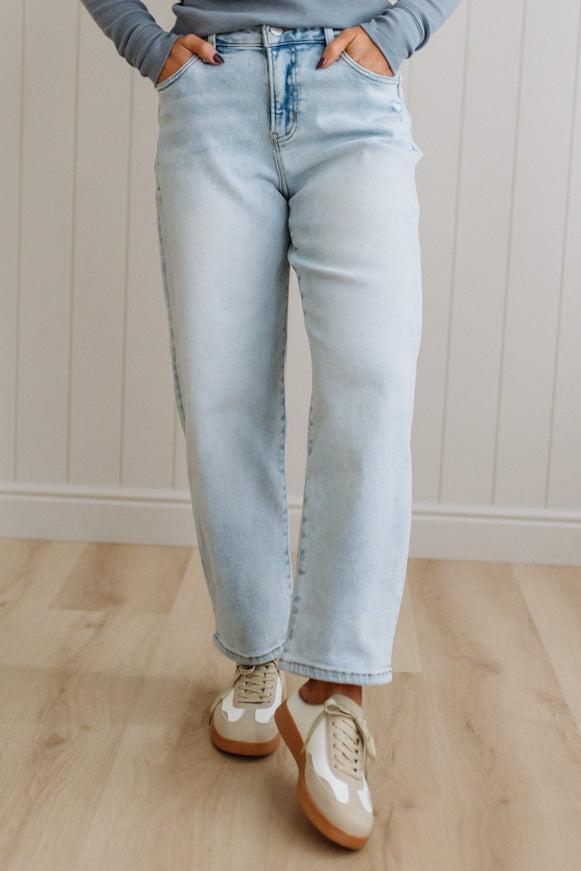 Person wearing light blue jeans and white sneakers on a wooden floor.