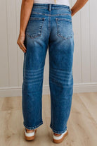 Person wearing blue jeans standing on a wooden floor with a white paneled wall in the background