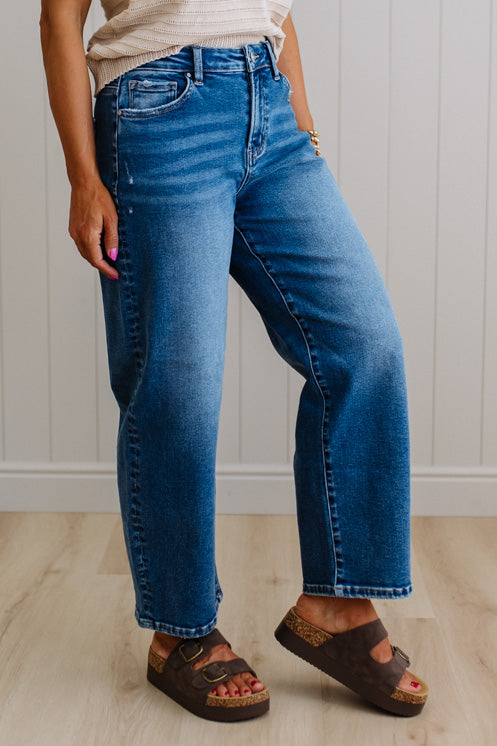 Person wearing blue jeans and brown sandals against a white paneled wall.