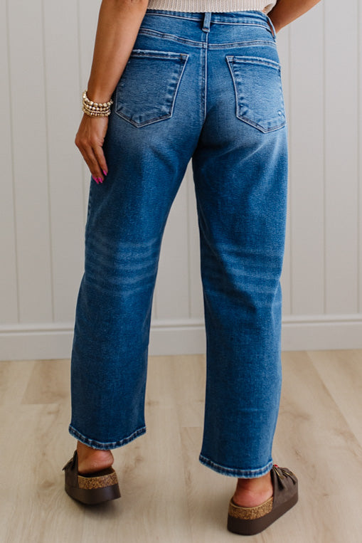 Person wearing blue jeans standing against a white paneled wall.