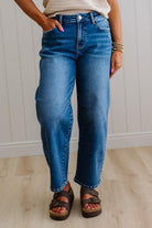 Person wearing blue jeans and sandals standing against a white paneled wall.