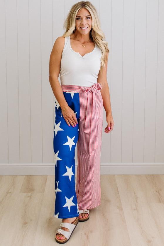 Woman wearing a white tank top and blue pants with white stars, standing against a white wall.