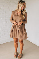 Woman wearing a brown dress standing against a white brick wall.