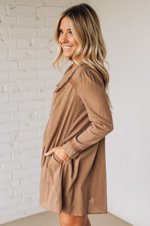 Woman wearing a brown dress against a white brick wall