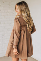 Woman wearing a brown dress against a white brick wall.