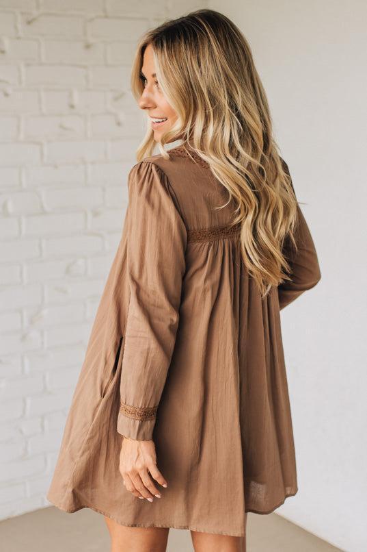 Woman wearing a brown dress against a white brick wall.