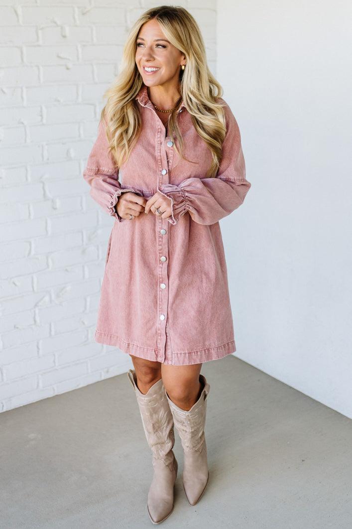 Woman wearing a pink dress and beige knee-high boots against a white brick wall.