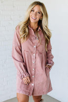 Woman wearing a pink denim dress against a white brick wall.