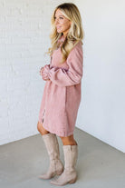 Woman wearing a pink dress and beige knee-high boots against a white brick wall.