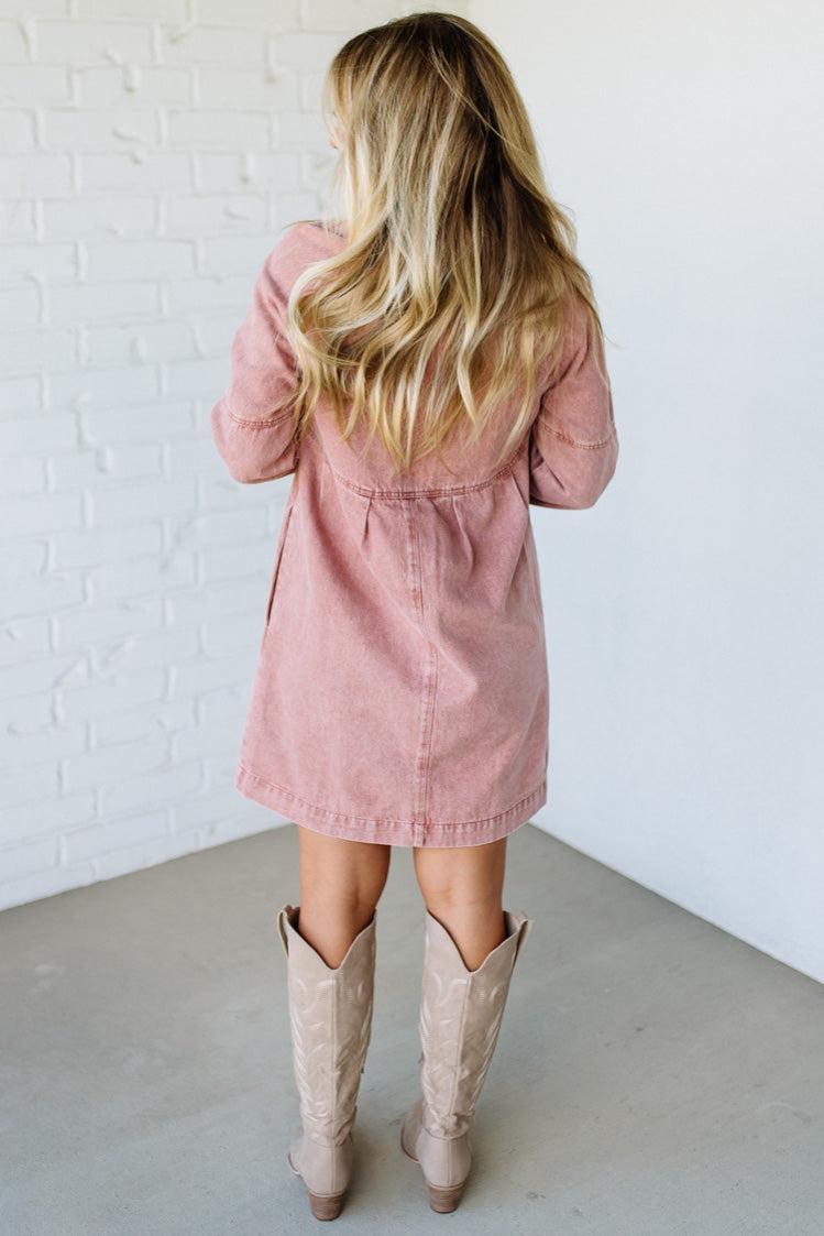 Person wearing a pink dress and beige cowboy boots against a white brick wall.