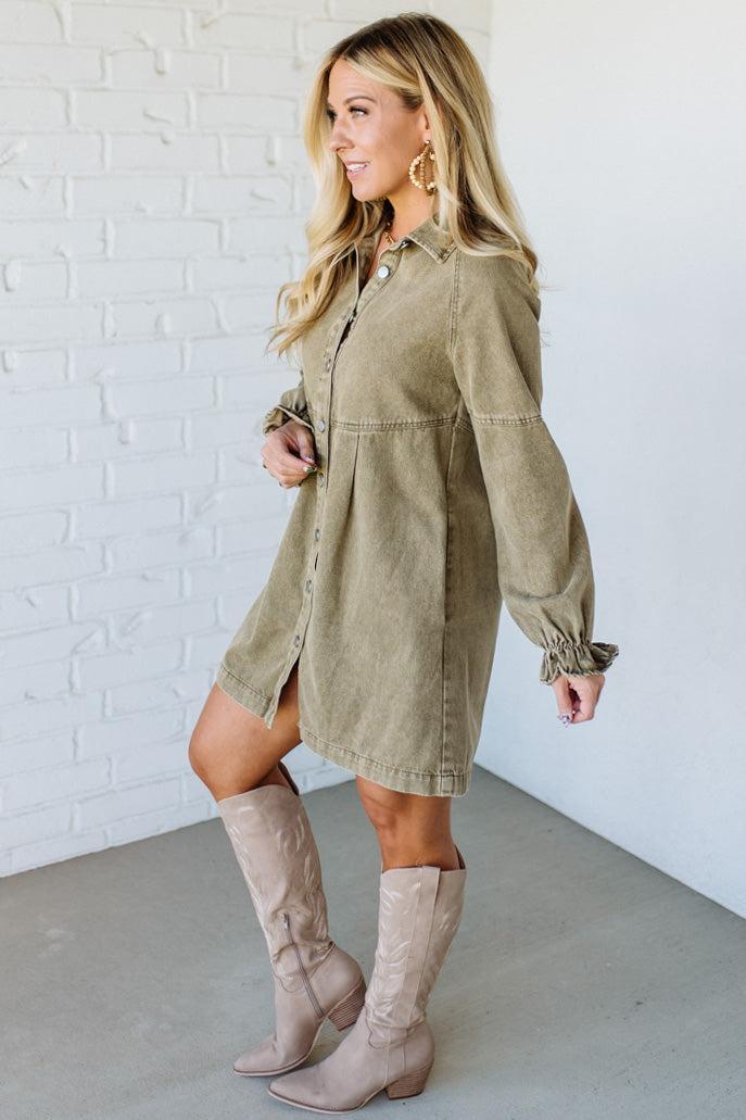 Woman wearing a green dress with long sleeves and beige knee-high boots against a white brick wall.