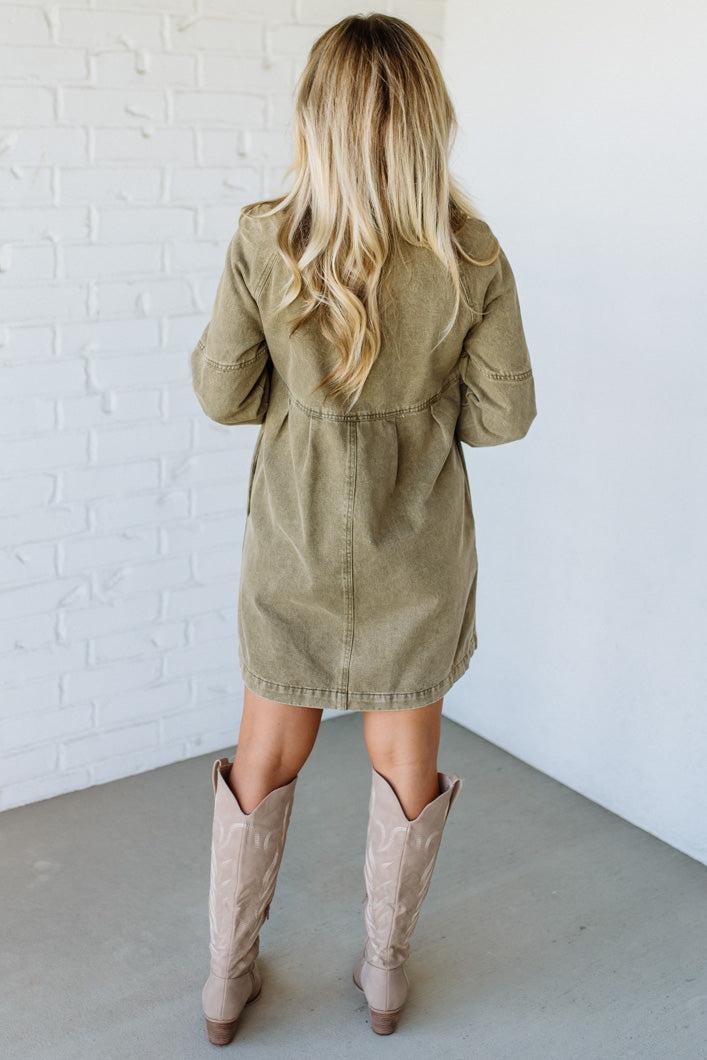 Woman wearing a beige trench coat and tan knee-high boots against a white brick wall.