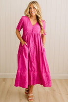 Woman wearing a pink dress standing against a white paneled wall.