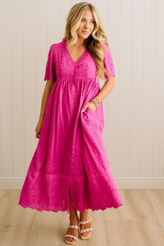Woman wearing a pink dress standing against a white wall.
