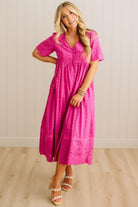 Woman wearing a bright pink dress standing against a light wooden panel background