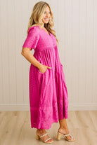 Woman wearing a pink dress standing against a white paneled wall.