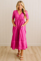 Woman wearing a pink dress standing against a white paneled wall.