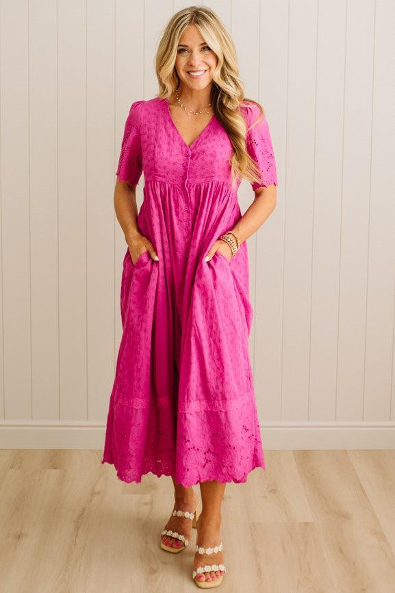 Woman wearing a pink dress standing against a white paneled wall.