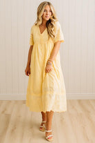 Woman wearing a yellow dress with lace details in a minimalistic setting.