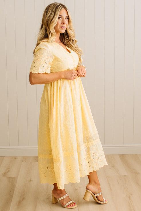 Woman wearing a yellow lace dress standing against a white paneled wall.