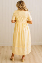 Woman wearing a yellow dress with lace details in a minimal indoor setting